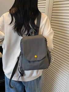 Minimalist grey canvas mini backpack with yellow button shown from a back view on model