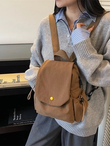 Brown canvas flap backpack with yellow button detail shown on a model for casual style