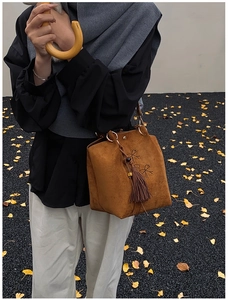 Détail du sac seau marron en suédine avec broderie florale et pompon sur gravier noir