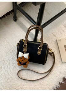 Detail of black matte suede pillow bag with brown leather handles and a cute bear charm