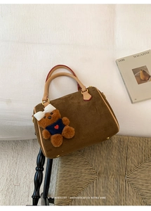 Close-up of brown matte suede Boston bag with a cute bear charm on woven texture