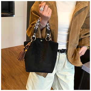 Détail du sac à main en daim noir avec nœuds brodés et poignée en motif pied-de-poule