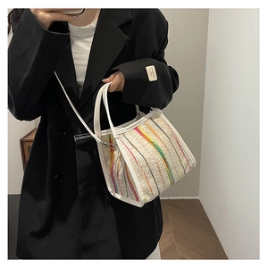 Detalle de un bolso trapecio de paja con rayas de colores y ribete de cuero sintético