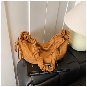Macro detail of brown pleated suede dumpling bag on a minimal book decor setting
