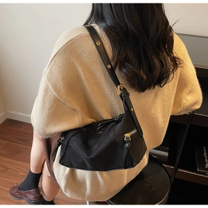 Detail view of black matte leather shoulder bag with golden hardware on a beige knit sweater