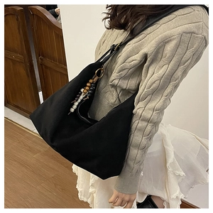 Detail of black crescent shoulder bag featuring a bohemian style wooden bead charm tassel