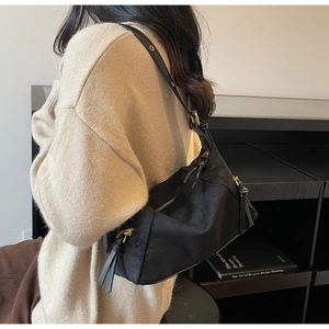 Detail view of black dumpling bag with matte texture and metallic zipper on model shoulder