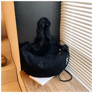 Detail of black suede dumpling bag with elegant ruffled shoulder strap on a book