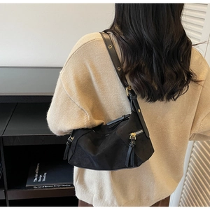 Close-up of black suede dumpling bag with adjustable strap and metallic gold eyelets