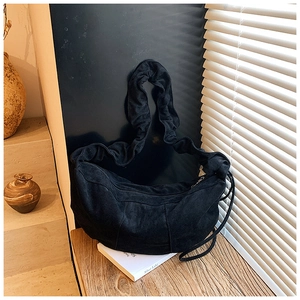 Detail of black suede crescent bag featuring ruffled shoulder strap and side fringe