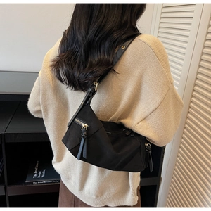 Detail view of a black minimalist nylon shoulder bag worn by a model in a cozy indoor setting