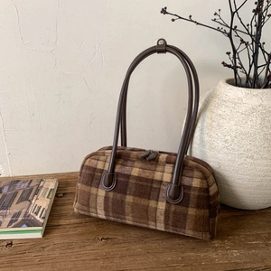 Detailed view of brown plaid tote bag with leather straps on a wooden table