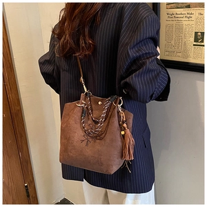 Détail d'un sac seau en daim marron avec nœud perlé, poignée tissée et glands en cuir