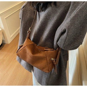 Detailed close-up of brown suede shoulder bag with metal zipper and tassel accent