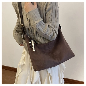Close-up of dark brown faux suede tote bag with colorful wooden beads on model