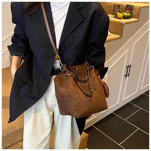 Détail du sac seau en daim marron avec poignée tressée, pompon et imprimé nœud