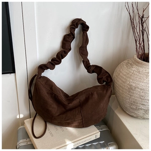 Detail of dark brown suede crescent bag with gathered shoulder strap on travel books