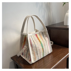Primer plano de un bolso tote tejido a rayas con bordados coloridos y asas de cuero blanco