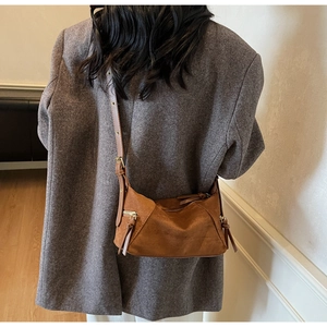 Brown suede dumpling bag worn over shoulder with adjustable strap and gold zipper detail
