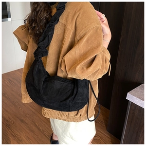 Detailed view of black faux suede pleated shoulder strap on a crescent bag