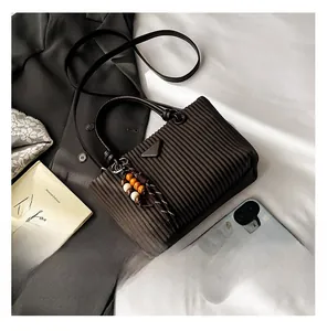 Détail d'un sac seau plissé marron foncé avec logo triangulaire et charm en perles ethniques