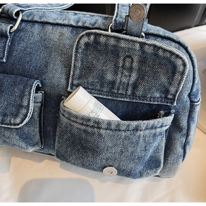 Detailed macro view of denim shoulder bag exterior pockets with vintage metal button fasteners