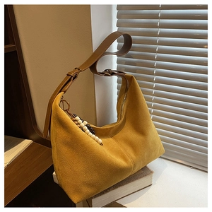 Détail du sac hobo en daim jaune sur des livres avec breloque en perles et sangle en cuir