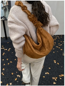 Detail of caramel suede hobo bag with pleated shoulder strap in autumn outdoor setting