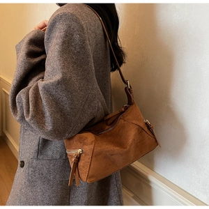 Close-up of retro brown suede shoulder bag showing textured material and metal zipper detail