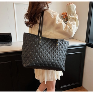 Detail of black quilted tote bag with golden rivets and elegant shoulder strap