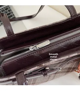 Macro detail of silver MSKK zipper on dark brown plaid shoulder bag with leather trim