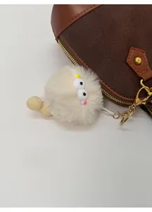 Detail of white plush monster keychain with big eyes on brown leather handbag