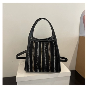 Detalle del bolso de cubo con rayas tejidas, asas de cuero negro y correa larga ajustable