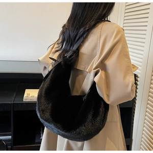 Close-up of black faux fur crescent shoulder bag with leather strap on a model's shoulder