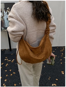 Back view of brown suede pleated dumpling bag shown on model in a minimalist outdoor setting