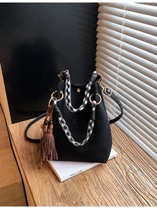 Sac seau noir minimaliste avec anse pied-de-poule et gland marron sur bureau en bois