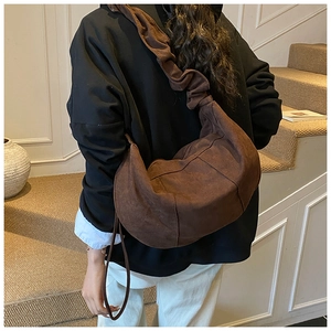 Deep brown crescent suede bag featuring wide pleated shoulder strap in a minimalist style