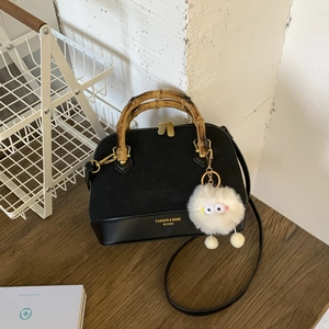 Detail of black shell bag with bamboo handle, matte texture, and plush charm on wood