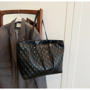 Detail of a large black tote bag with quilted diamond pattern and glossy leather finish