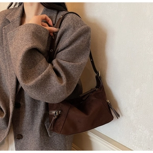 Detail of dark brown suede shoulder bag showing adjustable strap on gray blazer