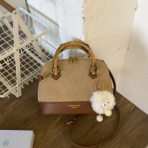 Detail of a retro color-block handbag featuring a bamboo handle and a plush monster charm