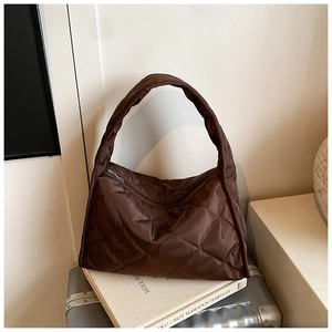 Detailed view of brown quilted puffer shoulder bag with silver zipper on a white book