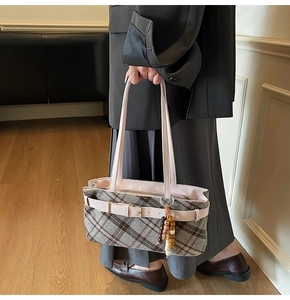 Detail of plaid handbag featuring wood bead charm and pink faux leather buckle strap