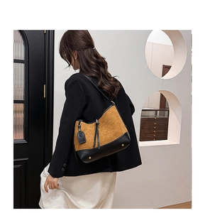 Detail of a brown suede crossbody bag with black leather trim and decorative tassel charm