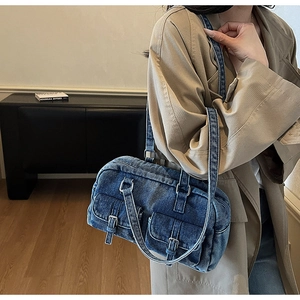 Detail of vintage blue denim shoulder bag with silver buckles and dual straps shown on a model