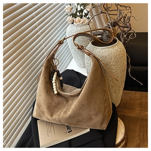 Détail d'un sac cabas en daim marron avec bandoulière en cuir et pendentif perlé élégant