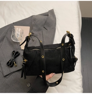 Detail of black suede dumpling bag with gold eyelets on shoulder strap and metal zipper