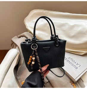 Gros plan d'un sac cabas noir plissé avec breloque en perles de bois et plaque métallique