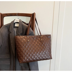 Detail of dark brown quilted tote bag with gold rivets hanging on a grey suit blazer