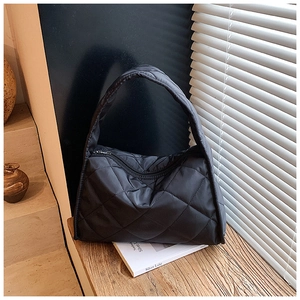 Detail of black quilted shoulder bag with diamond stitching and metal zipper on wooden table